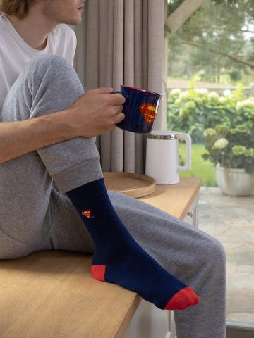 Mężczyzna w granatowych skarpetkach Superman trzymający kubek z logo tego bohatera